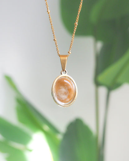 Back of Ivory White Eye of Saint Lucia Gold Necklace with green plant background, 18k gold stainless steel shiva eye pendant necklace, Saint Lucy Eye, operculum pendant