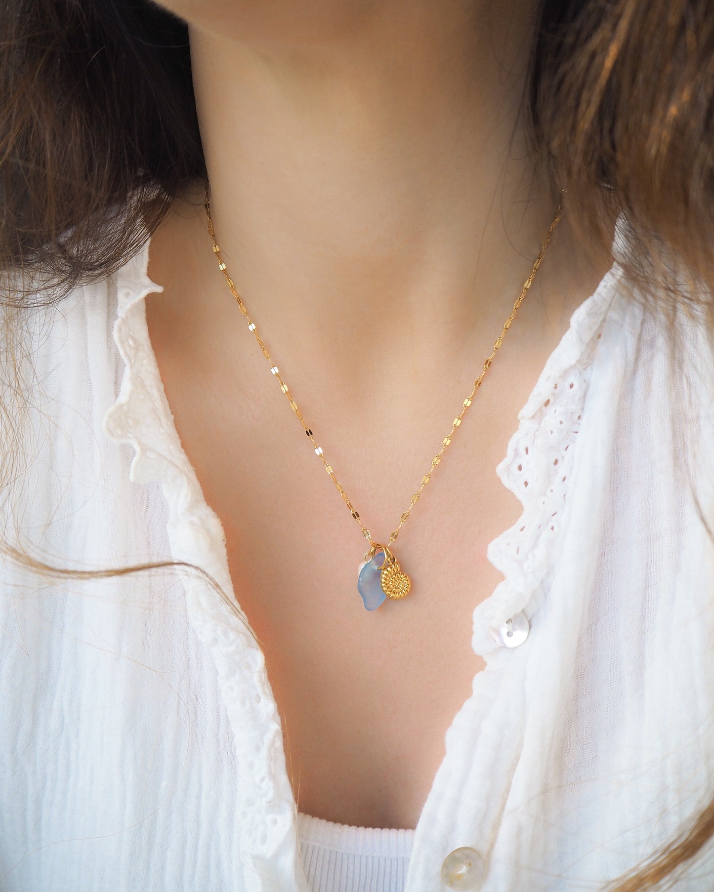 Model wearing Oceanic Trio Nautilus Blue Sea Glass Pearl Necklace on neck, nautilus shell necklace, ocean blue necklace, coastal jewelry, freshwater pearl necklace, gold seashell necklace, ocean-inspired jewelry, beach necklace, ocean treasure necklace