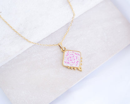 Close up of Portuguese Tile Necklace Floral Pink Gold on stone displayed. Made with 18k gold stainless steel and white pink floral pendant inspired by the Portuguese Azulejo design pattern. 