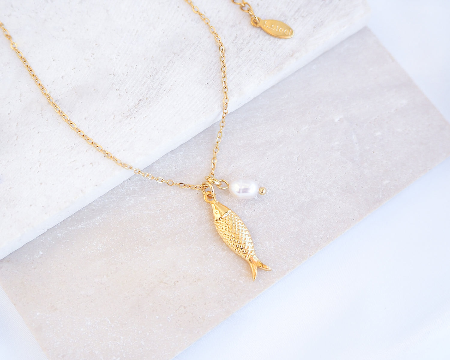 Gold Sardine Fish necklace with freshwater pearl on a marble surface
