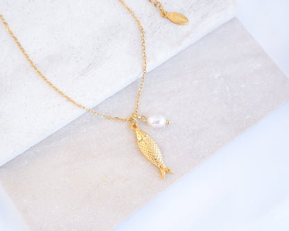 Gold Sardine Fish necklace with freshwater pearl on a marble surface