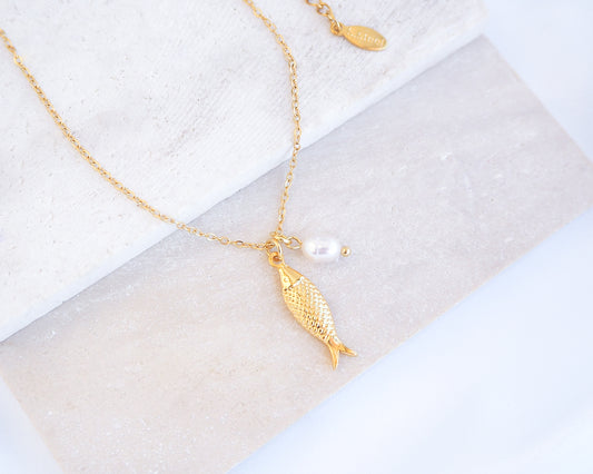 Gold Sardine Fish necklace with freshwater pearl on a marble surface