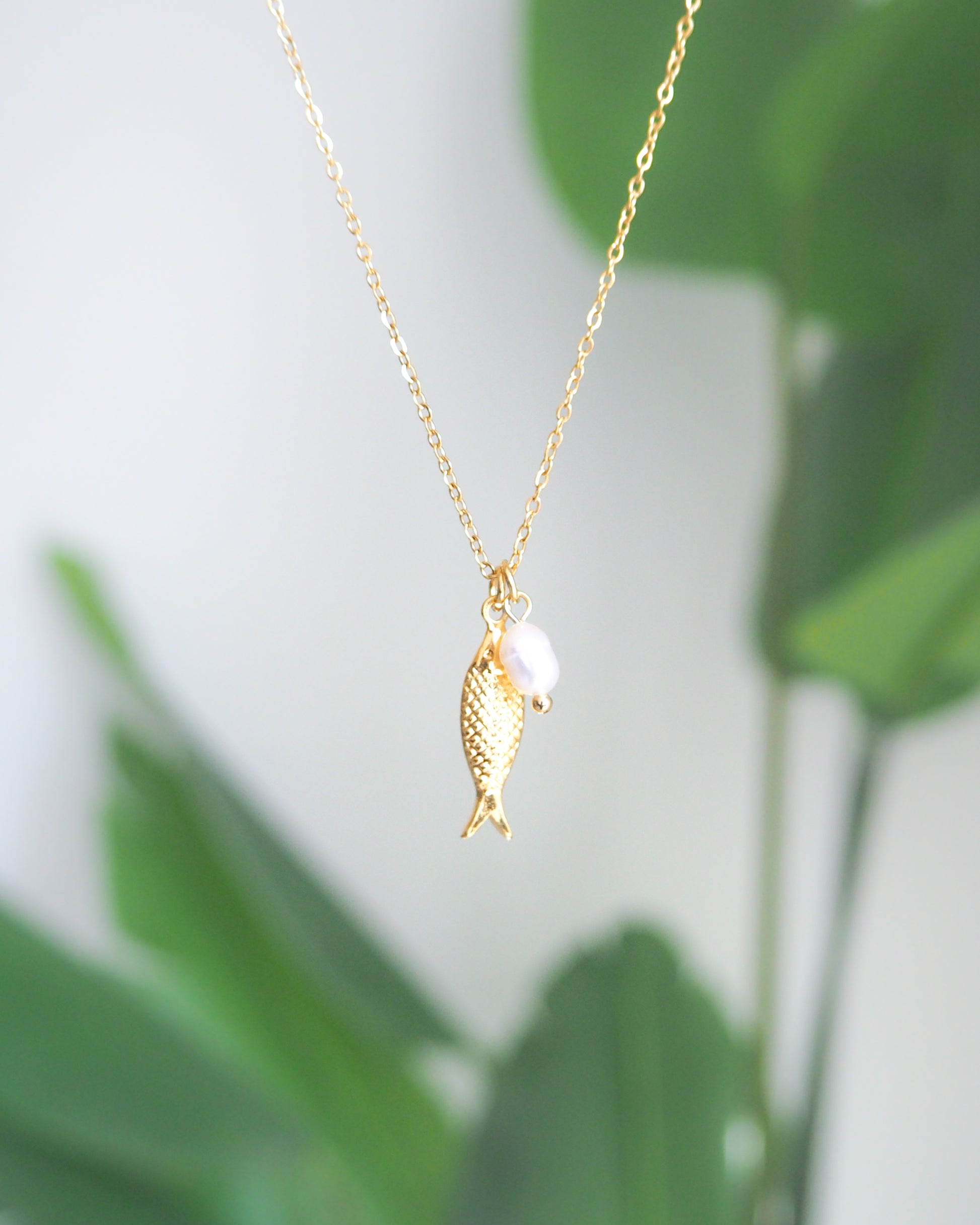 Gold Sardine Fish necklace with freshwater pearl with plant background 