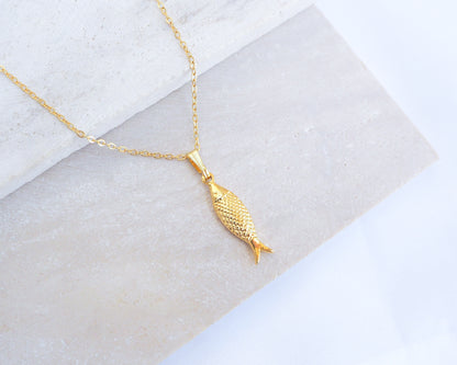 Gold Sardine Fish pendant necklace on a marble surface