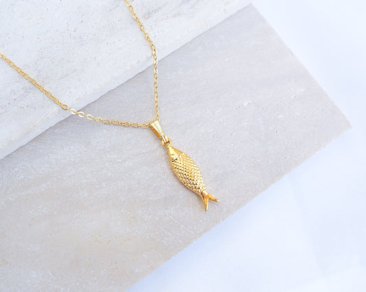 Gold Sardine Fish pendant necklace on a marble surface