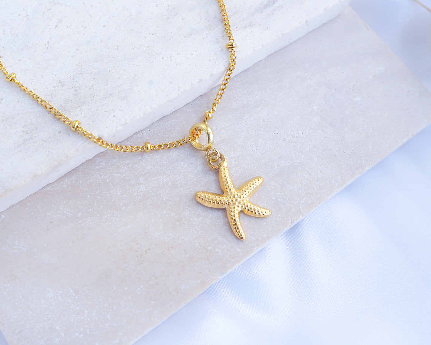 Gold Starfish Sea Star Necklace displayed on stone with dot chain gold necklace. 