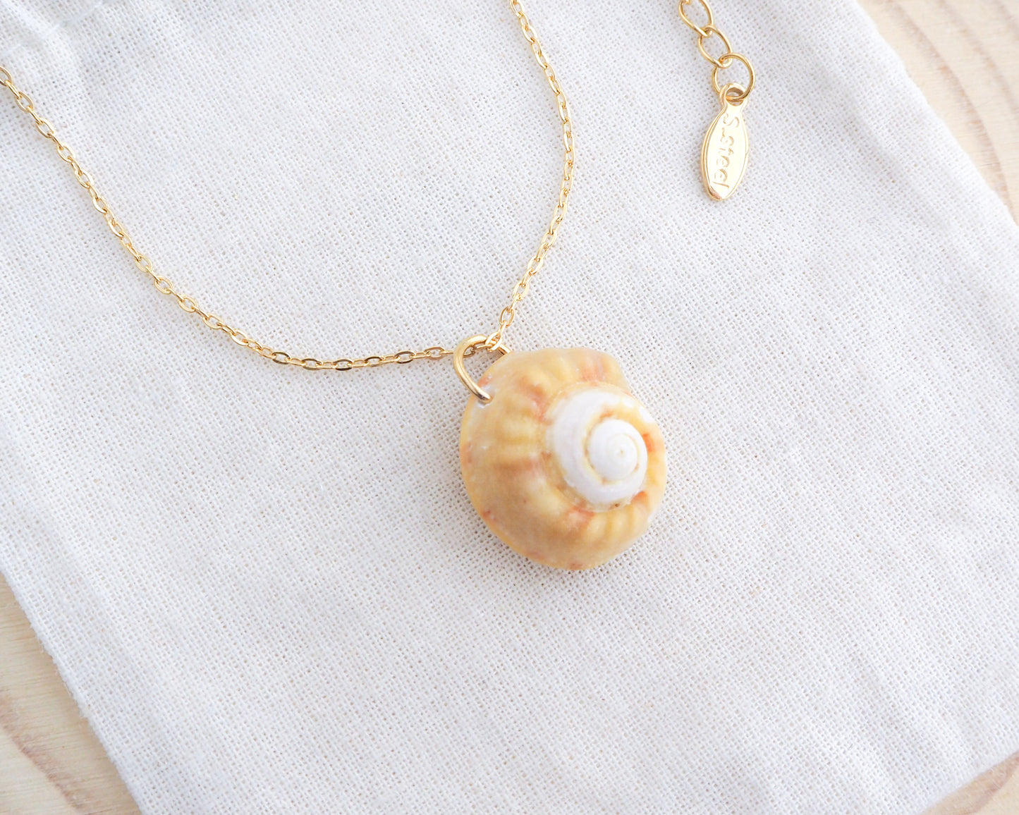 Side view of Sunny Magus Top Shell Necklace on display. A gold chain necklace with a delicate orange seashell pendant. The seashell is a orange in colour with a white interior. It's a handpicked magus top shell from the beach of Portugal.