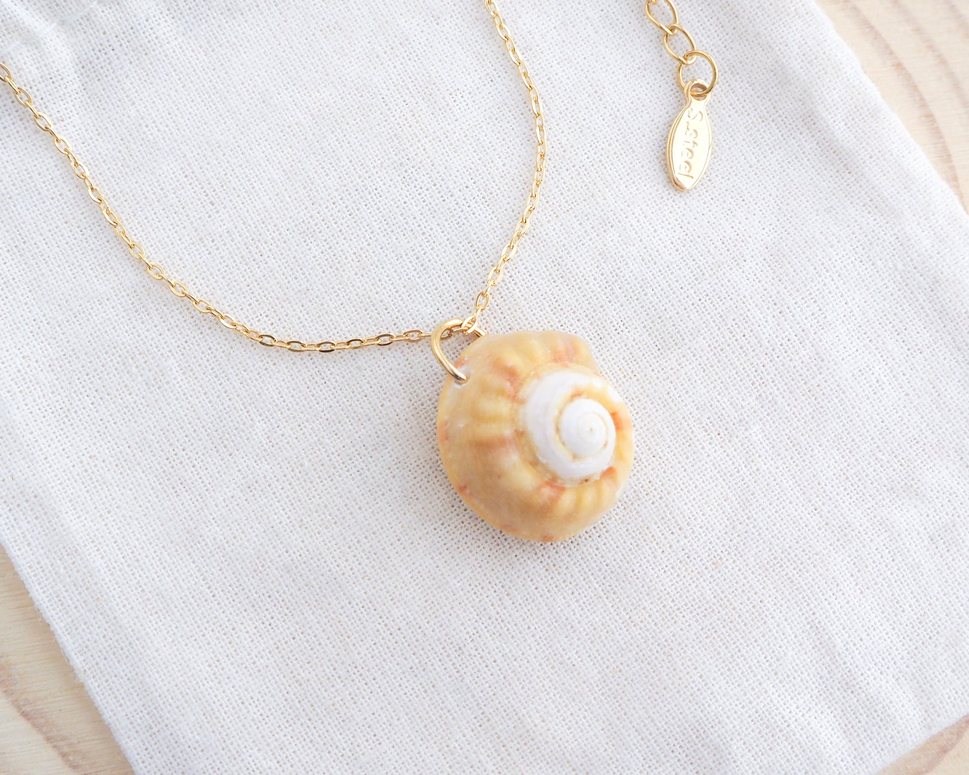 Side view of Sunny Magus Top Shell Necklace on display. A gold chain necklace with a delicate orange seashell pendant. The seashell is a orange in colour with a white interior. It's a handpicked magus top shell from the beach of Portugal.