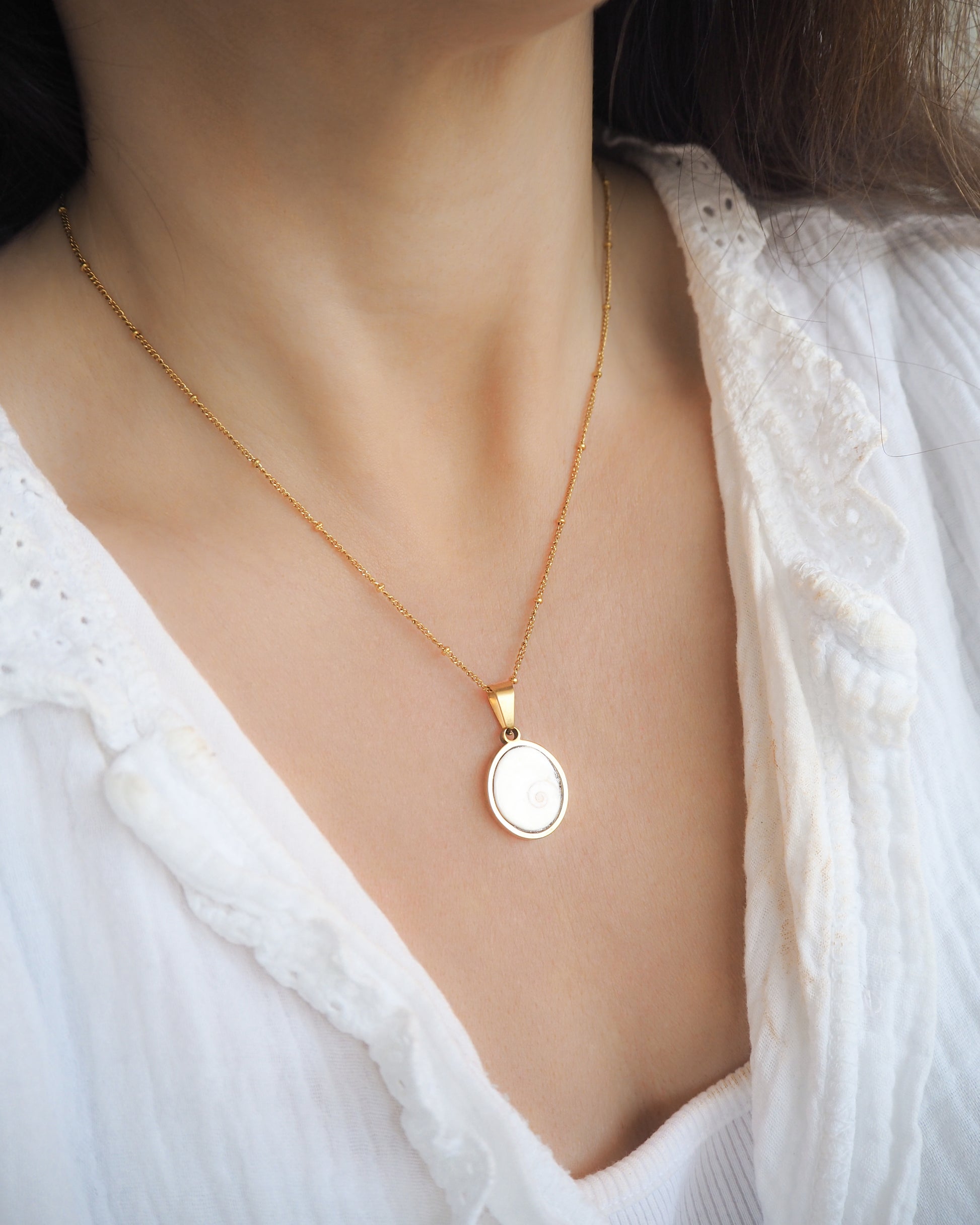 Model wearing White Eye of Saint Lucia Gold Necklace on neck, 18k gold stainless steel shiva eye pendant necklace, Saint Lucy Eye, operculum pendant
