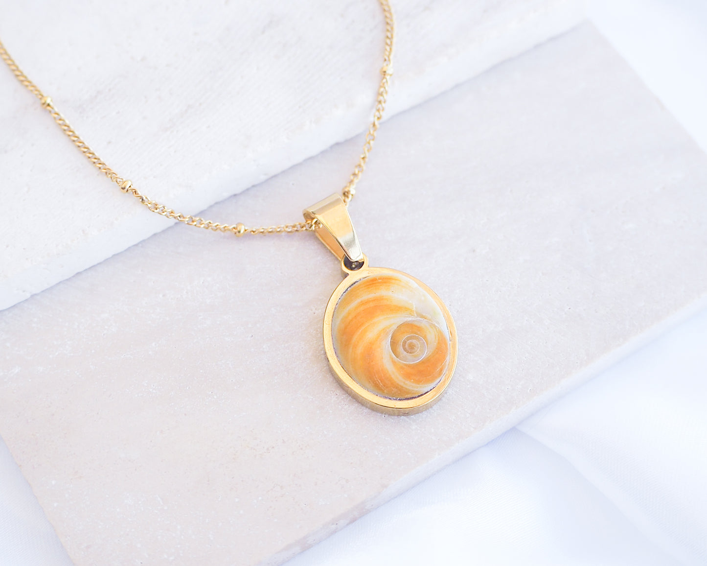 Gold Yellow Orange Shiva Eye, Eye of Saint Lucia Gold Necklace on stone displayed, 18k gold stainless steel shiva Yellow Orange eye pendant necklace, Saint Lucy Eye, operculum pendant