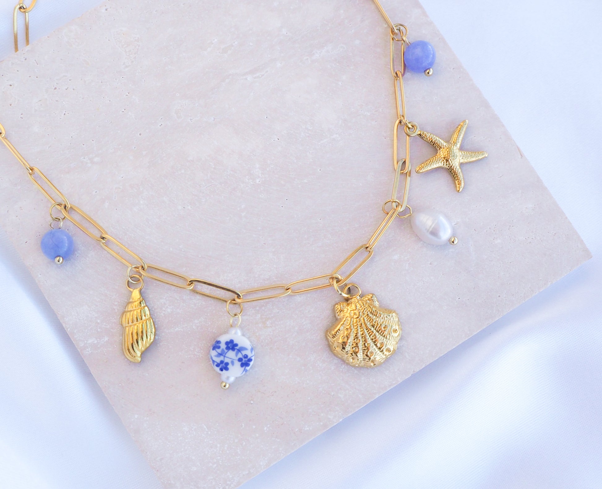 Oceanic Charm Necklace with Shells and Starfish Pendants, Freshwater Pearls and Gemstones on stone