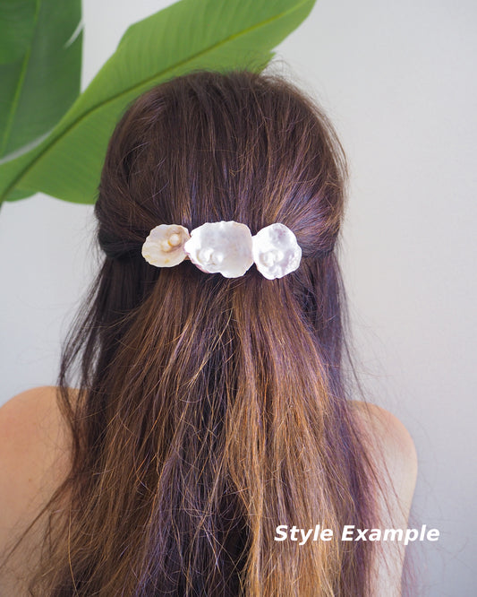 Model wearing Pearl oyster shell hair clip with pearls on in brown long hair with green plant and white background. Made with handpicked jingle shells saddle oysters from Portugal. Jingle Shell Pearl Hair clip. pearly shell Hair Clip Barrette on stone displayed, Boho Seashell Beach Clip from Portugal, Handpicked Real Shells, Seashell Hair Decoration, Bohemian Seashell Wedding Hair accessories, Coastal Christmas gift, Beach Wedding Hair
