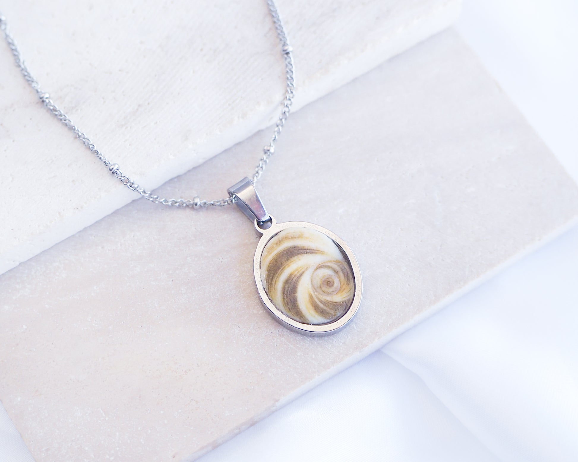 Khaki Green Eye of Saint Lucia Silver Necklace front view displayed on stone, silver stainless steel shiva eye pendant necklace, Saint Lucy Eye, operculum pendant