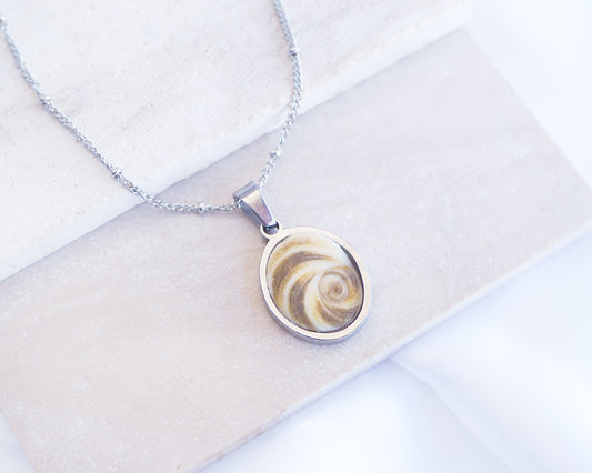 Khaki Green Eye of Saint Lucia Silver Necklace front view displayed on stone, silver stainless steel shiva eye pendant necklace, Saint Lucy Eye, operculum pendant