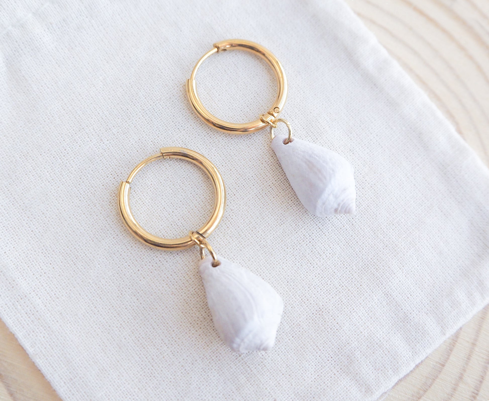 Close up of Light Mediterranean Cone Shell Gold Earring Hoops on displayed, handpicked cone shells from Portugal, 18k gold stainless steel shell earring hoops, seabylou 