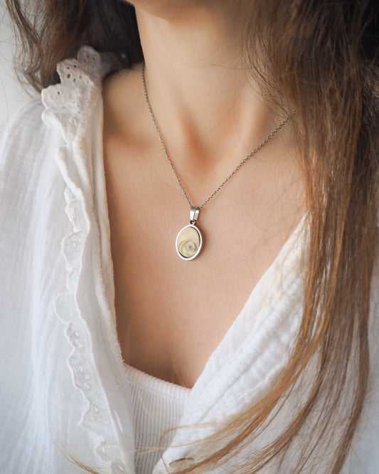 Model wearing Light Eye of Saint Lucia Silver Necklace on neck with white blouse and brown hair, silver stainless steel shiva eye pendant necklace, Saint Lucy Eye, operculum pendant