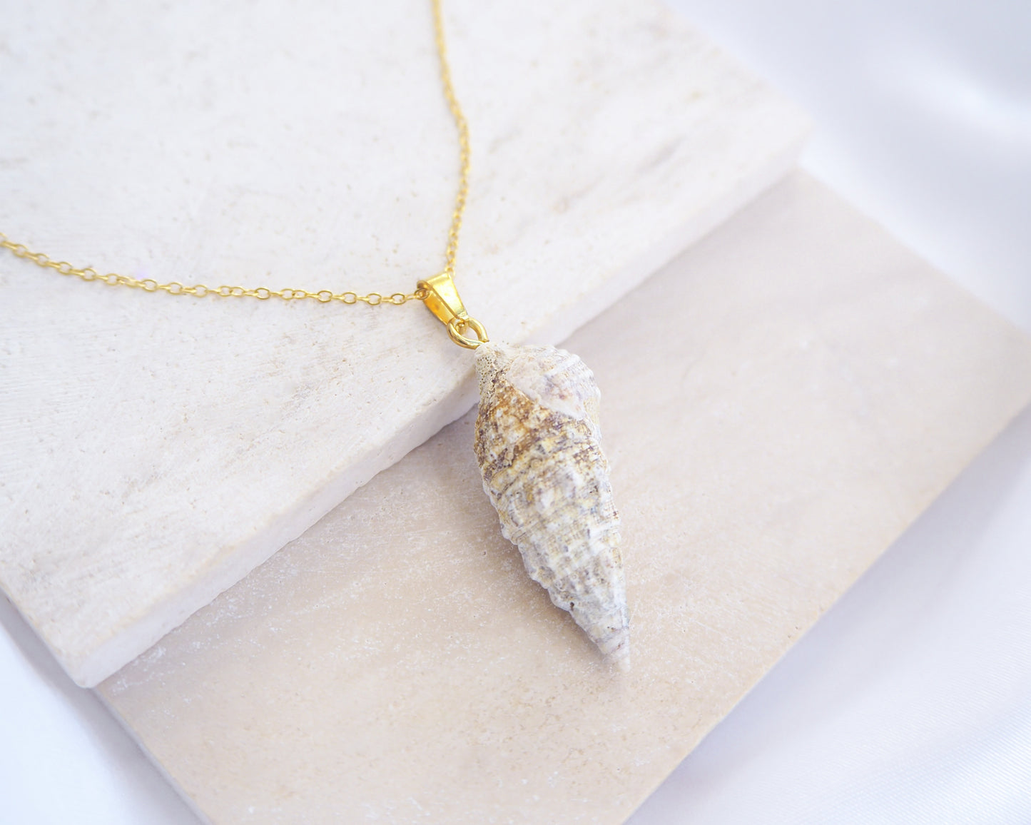 Close up of front view of Ivory Horn Shell Necklace on stone displayed. Made with 18k gold stainless steel 