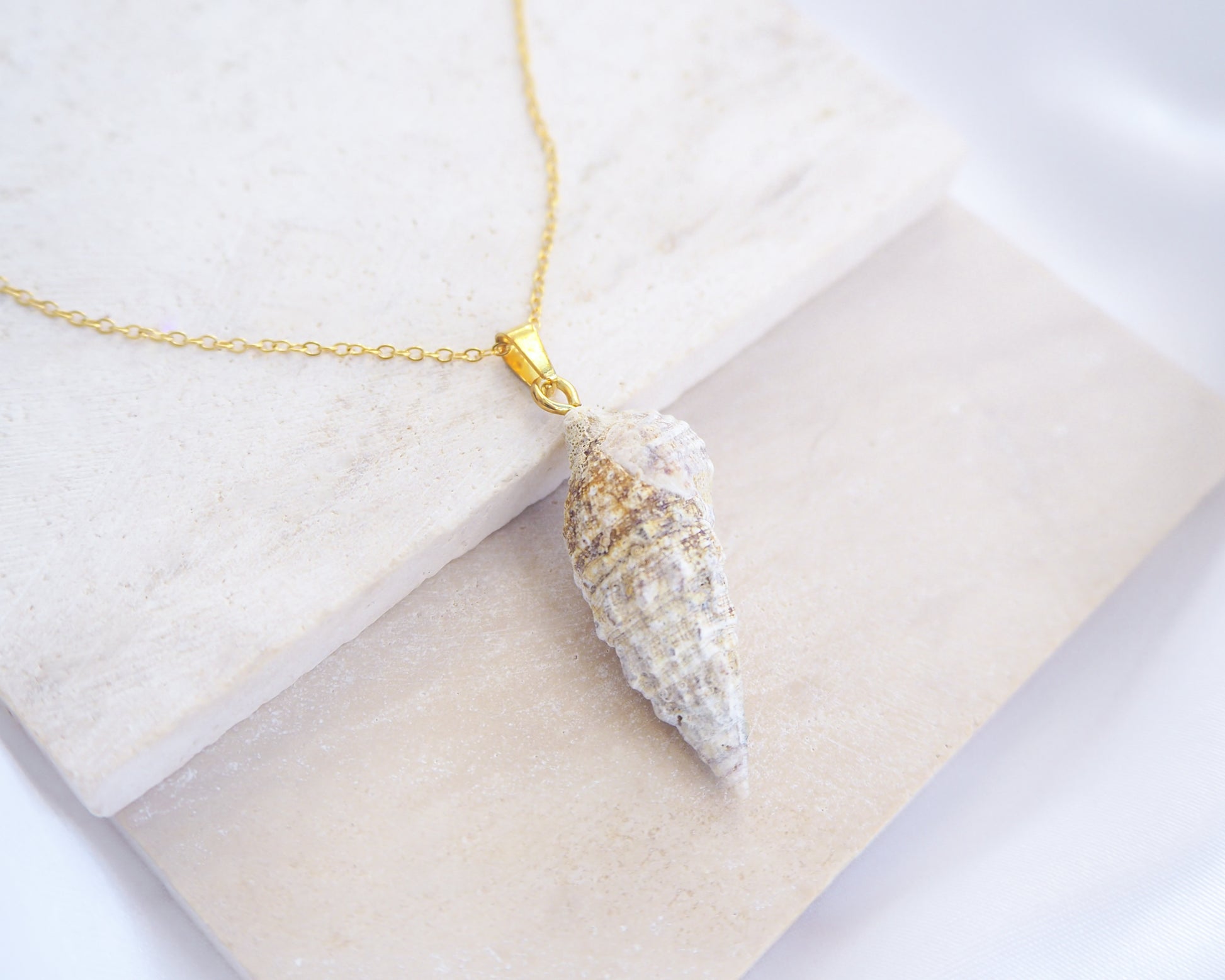 Close up of front view of Ivory Horn Shell Necklace on stone displayed. Made with 18k gold stainless steel 