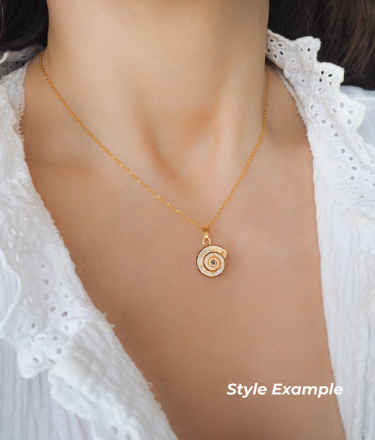 Gold necklace with a spiral pendant worn by a person in a white lace top.