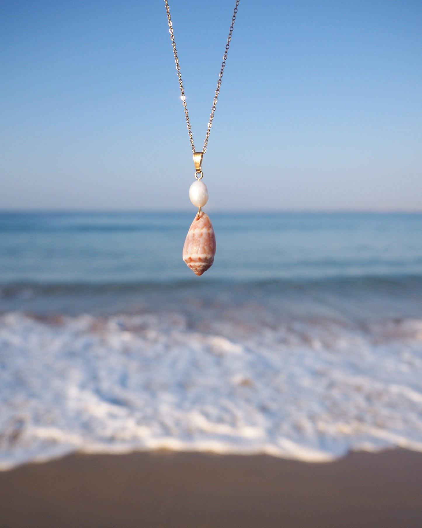 Front view of Mediterranean Cone Shell Pearl Necklace with ocean background, handpicked cone shell from Algarve, Freshwater pearl and 18k gold stainless steel chain