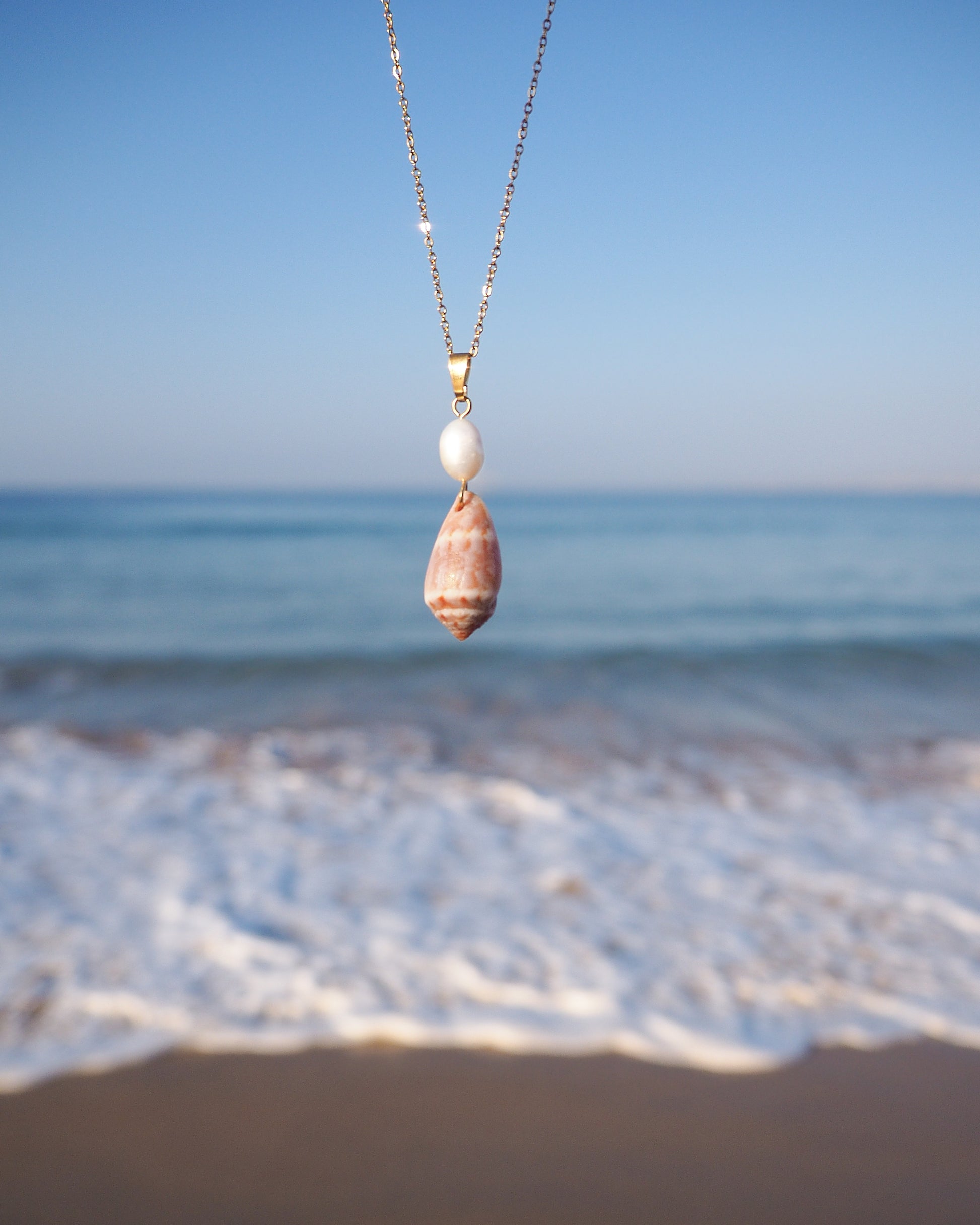 Front view of Mediterranean Cone Shell Pearl Necklace with ocean background, handpicked cone shell from Algarve, Freshwater pearl and 18k gold stainless steel chain