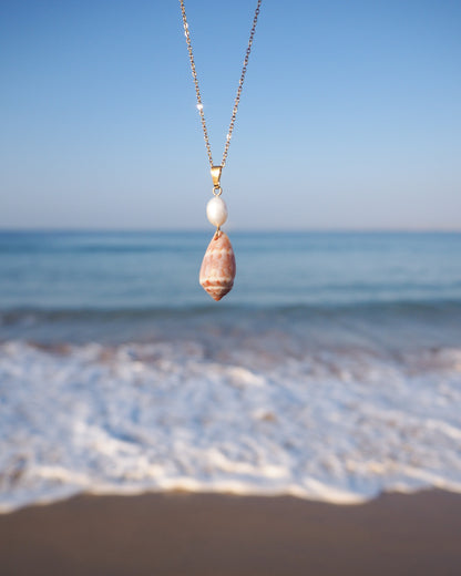 Front view of Mediterranean Cone Shell Pearl Necklace with ocean background, handpicked cone shell from Algarve, Freshwater pearl and 18k gold stainless steel chain