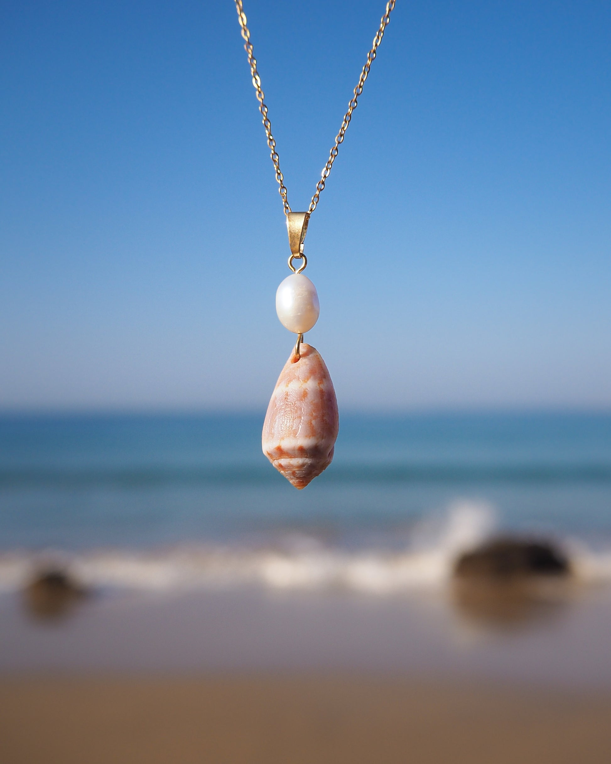 Mediterranean Cone Shell Pearl Necklace from Portugal front view with ocean background, handpicked cone shell from Algarve, Freshwater pearl and 18k gold stainless steel chain