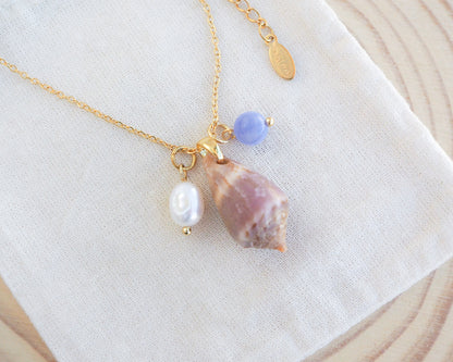 Close up of gold necklace with medium cone shell and a gemstone and pearl necklace on display. Mediterranean cone shell was handpicked from Portugal. Made with a ivory white freshwater pearl and blue angelite gemstone bead. Made with 18k gold stainless steel clasp and necklace chain. 