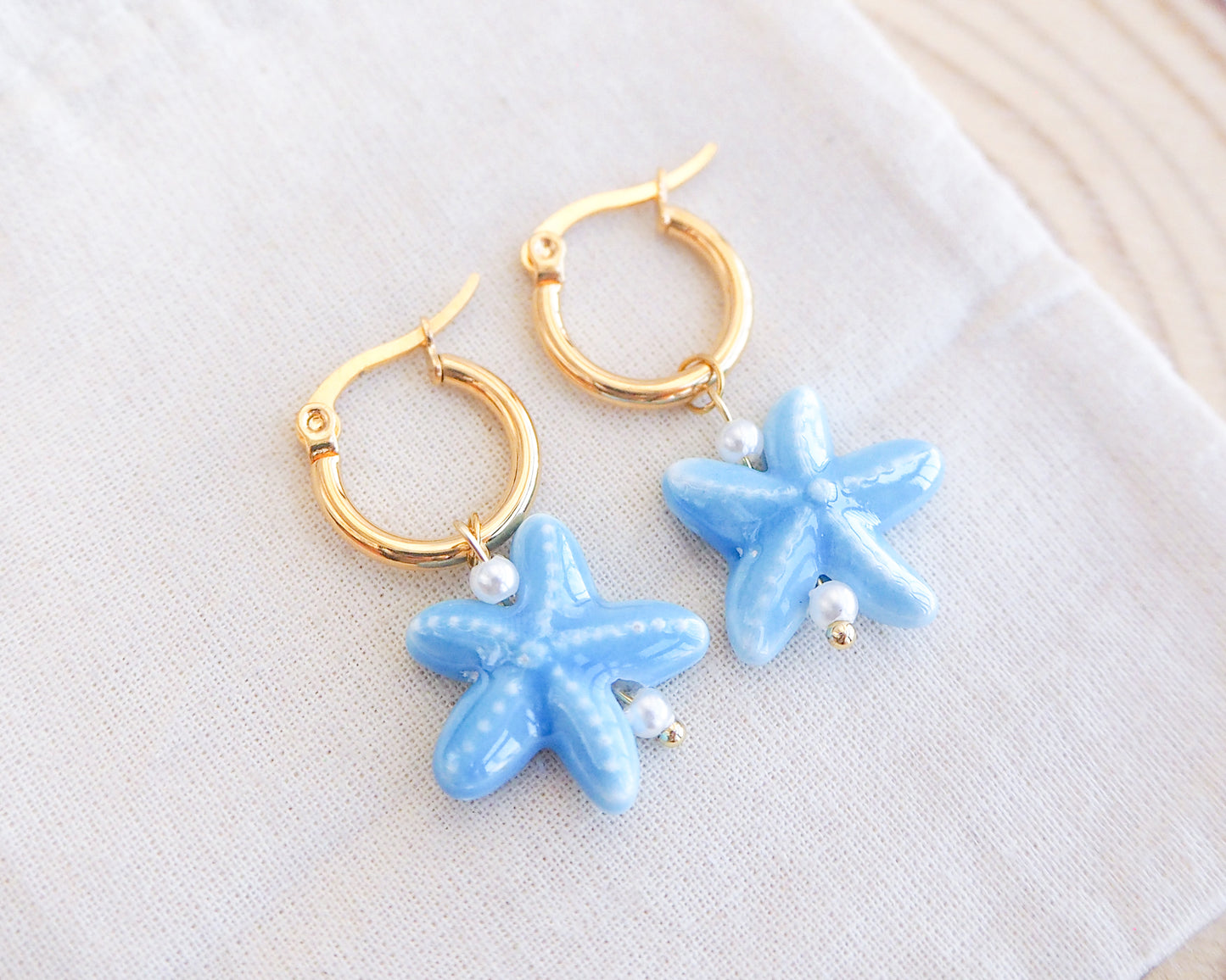 Gold ceramic blue sea star earrings made with 14k gold stainless steel and blue ceramic starfish charms on stone displayed