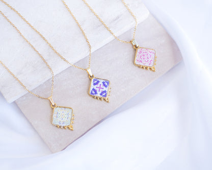 Mix of Portuguese Tile Necklaces on stone displayed. Made with 18k gold stainless steel and silver stainless steel. Showcasing white pink floral pendant, a green floral pendant and a purple pink floral pendant inspired by the Portuguese Azulejo design pattern. 