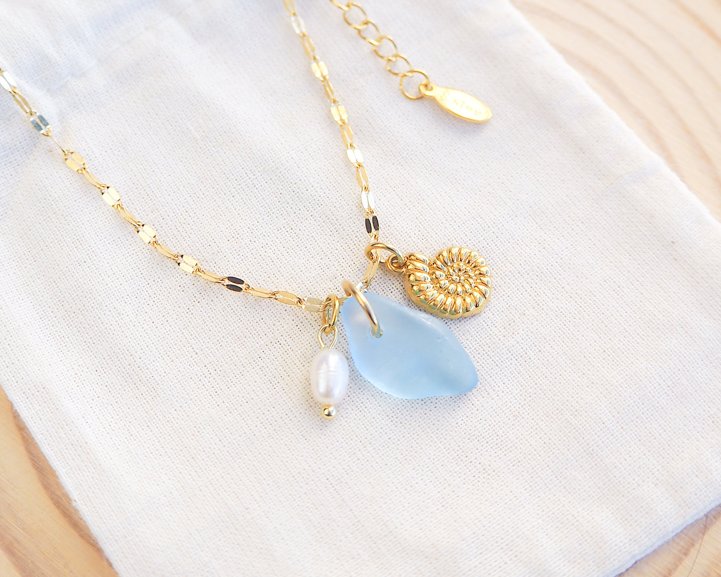 Front view of Oceanic Trio Nautilus Blue Sea Glass Pearl Necklace on display, nautilus shell necklace, ocean blue necklace, coastal jewelry, freshwater pearl necklace, gold seashell necklace, ocean-inspired jewelry, beach necklace, ocean treasure necklace
