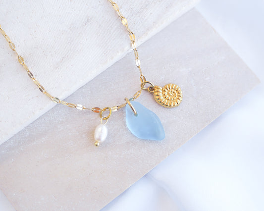 Oceanic Trio Nautilus Blue Sea Glass Pearl Necklace on stone displayed, nautilus shell necklace, ocean blue necklace, coastal jewelry, freshwater pearl necklace, gold seashell necklace, ocean-inspired jewelry, beach necklace, ocean treasure necklace