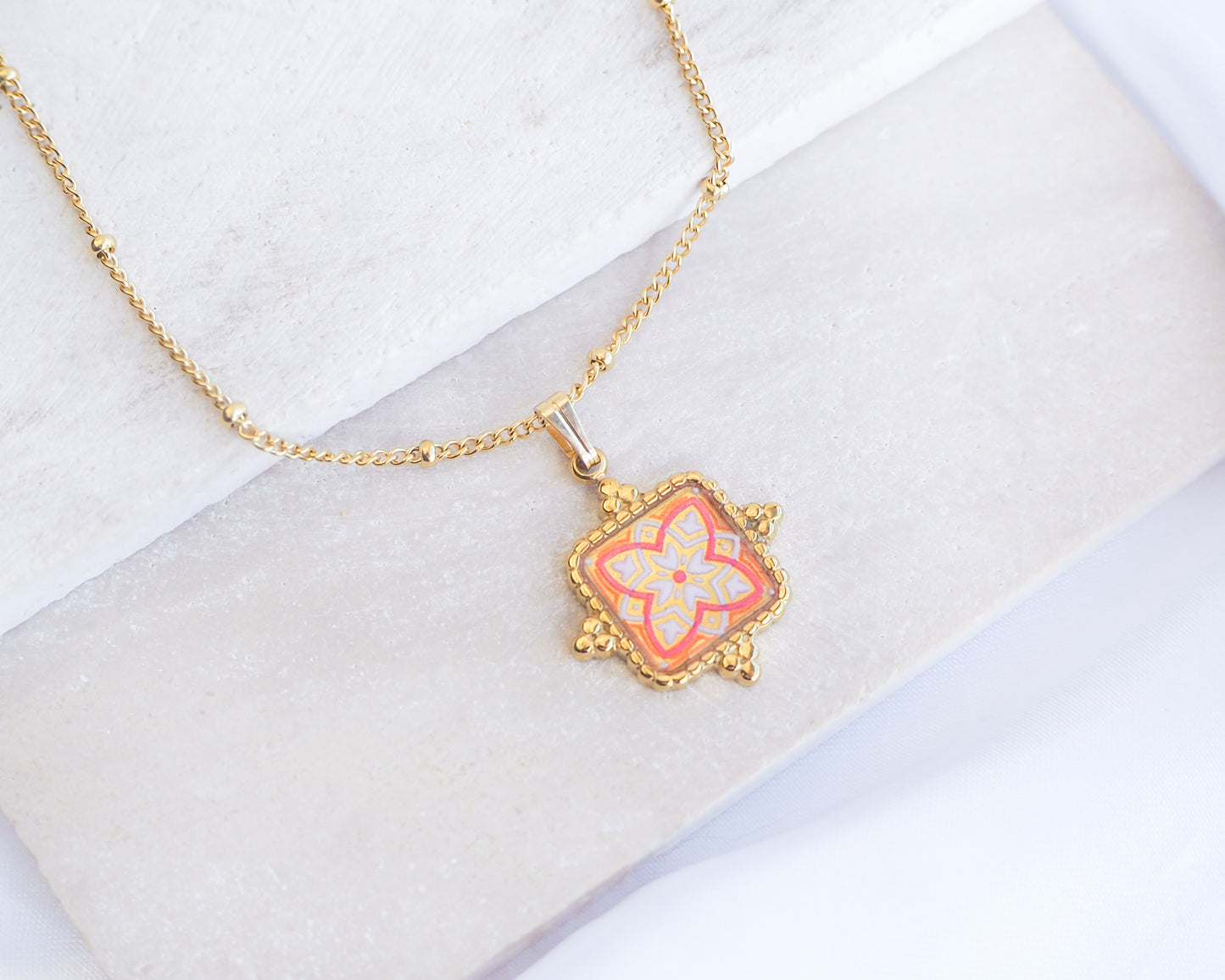 Close up of Orange Portuguese Tile Square Necklaces Gold on stone displayed. Made with 18k gold stainless steel and white blue mosaic pendant inspired by the Portuguese Azulejo design pattern. 