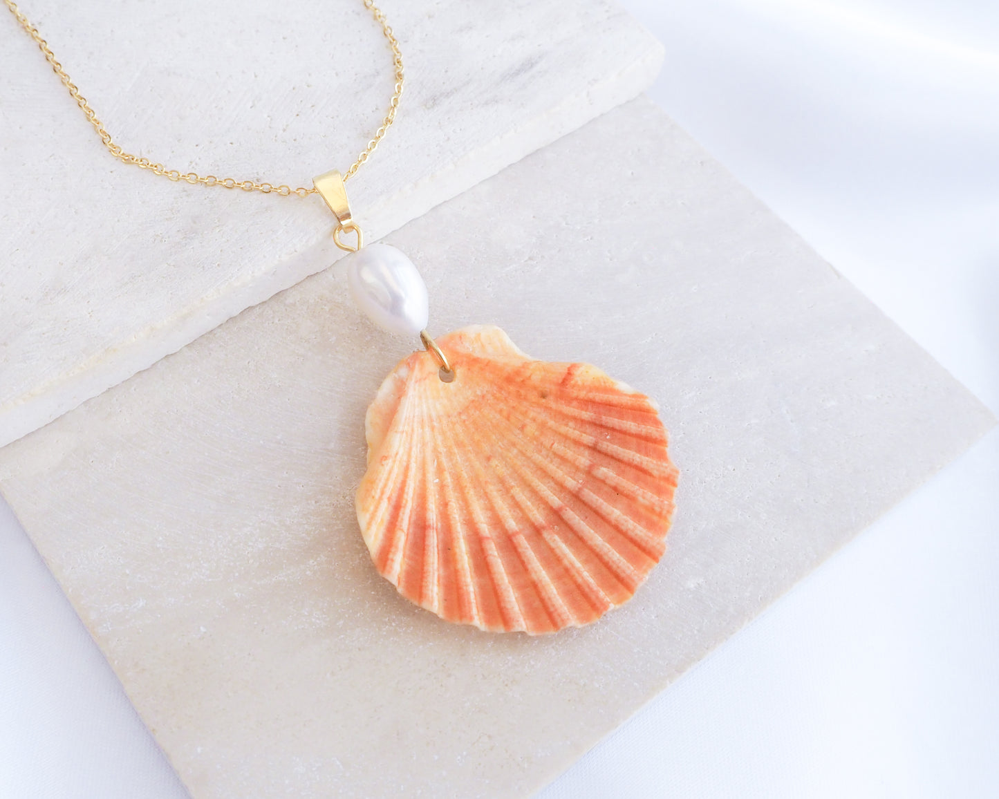 Close up of Orange Scallop Shell Pearl Gold Necklace V on stone displayed, Pilgrims Scallop Shell from Portugal with freshwater pearl and gold chain. 