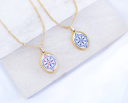 Two gold Portuguese Tile Oval Necklaces on a white stone surface. Made with 18k gold stainless steel and white blue mosaic pendant inspired by the Portuguese Azulejo design pattern. 