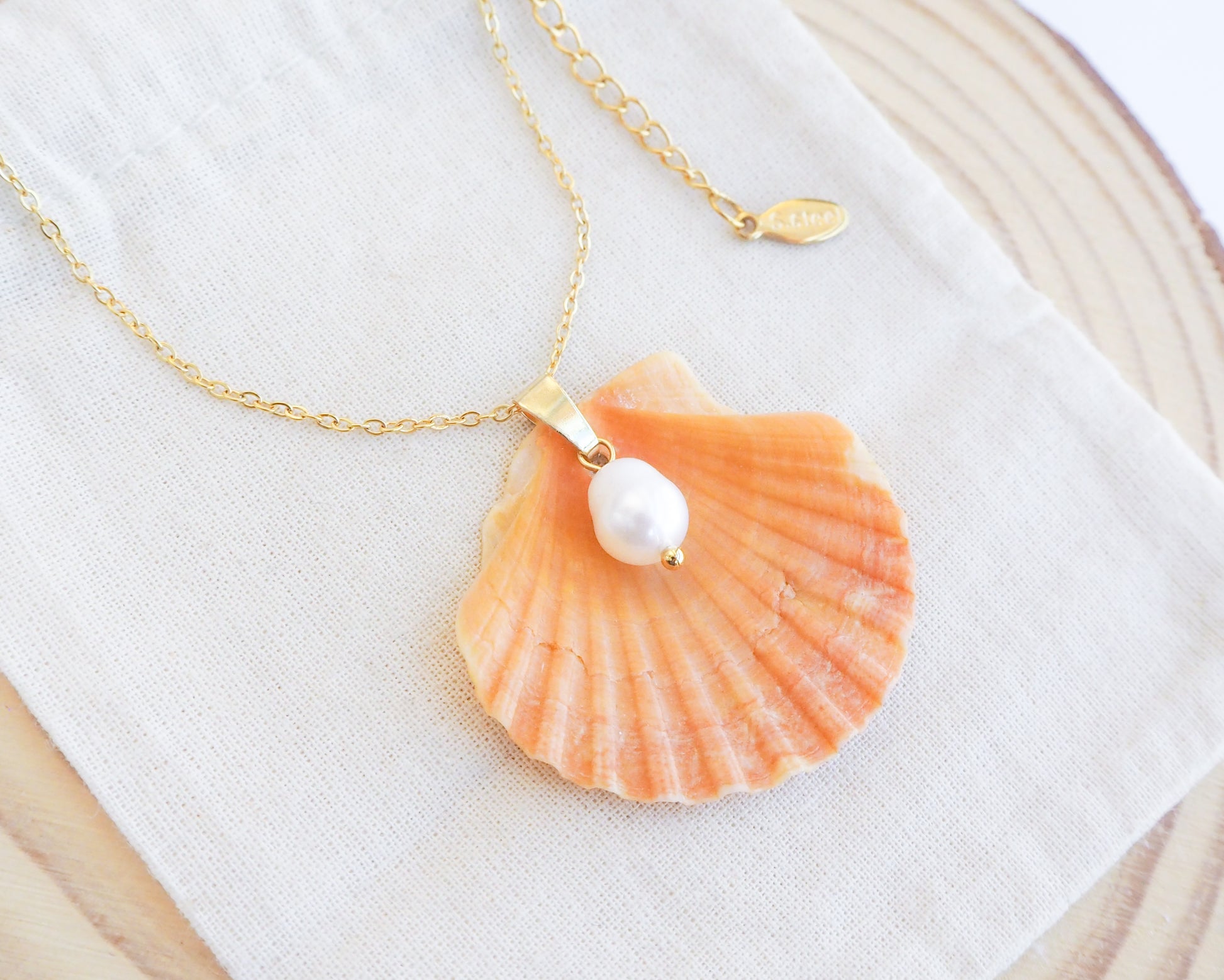 Close up of Coral Orange Scallop Shell Pearl Gold Necklace II on display, Pilgrims Scallop Shell from Portugal with freshwater pearl and gold chain. 