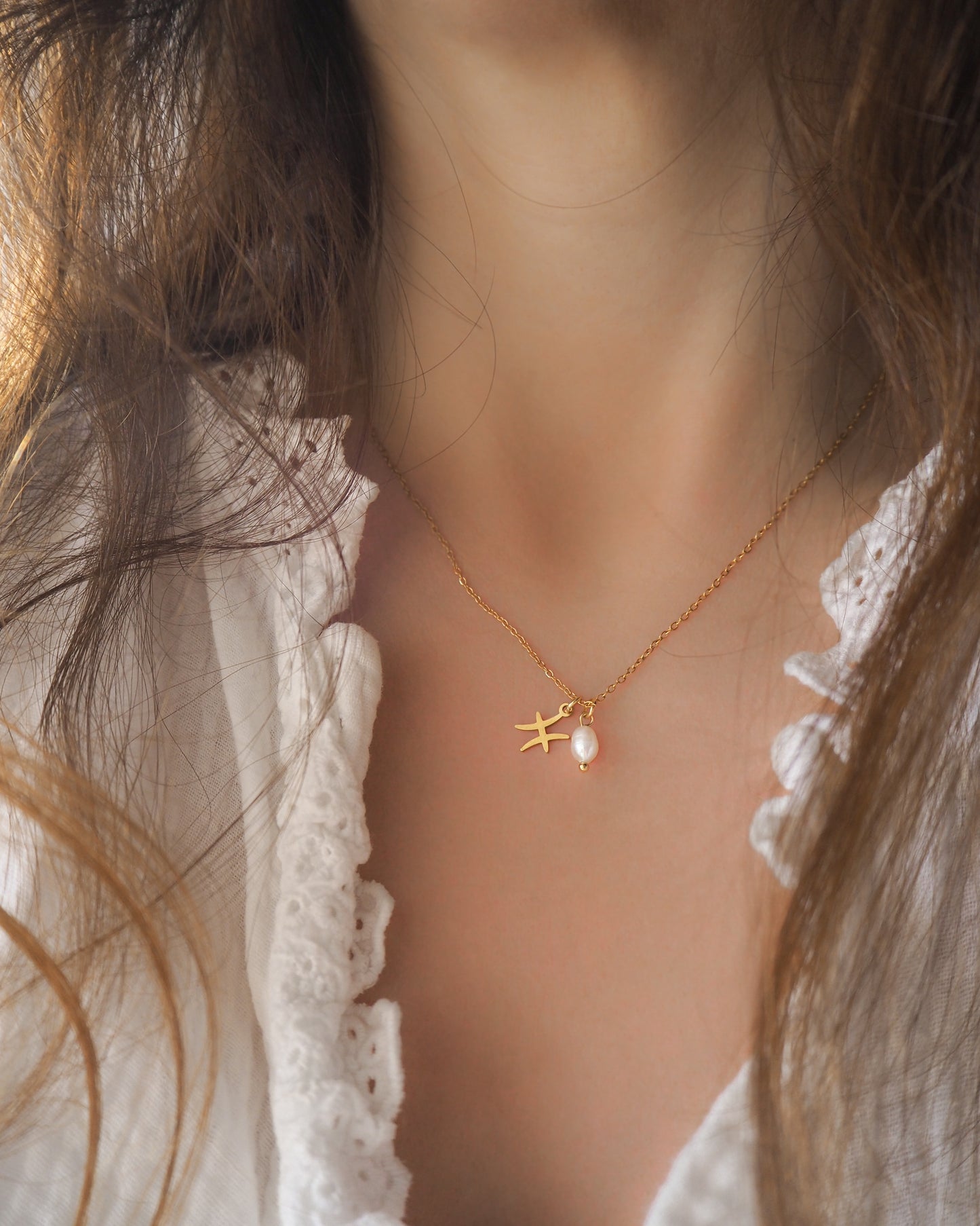 Model wearing Gold Pisces Zodiac Pearl Necklace on neck with brown hair, made with 18k gold stainless steel and white freshwater pearl 