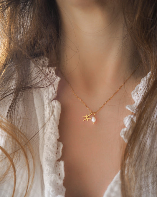 Model wearing Gold Pisces Zodiac Pearl Necklace on neck with brown hair, made with 18k gold stainless steel and white freshwater pearl 