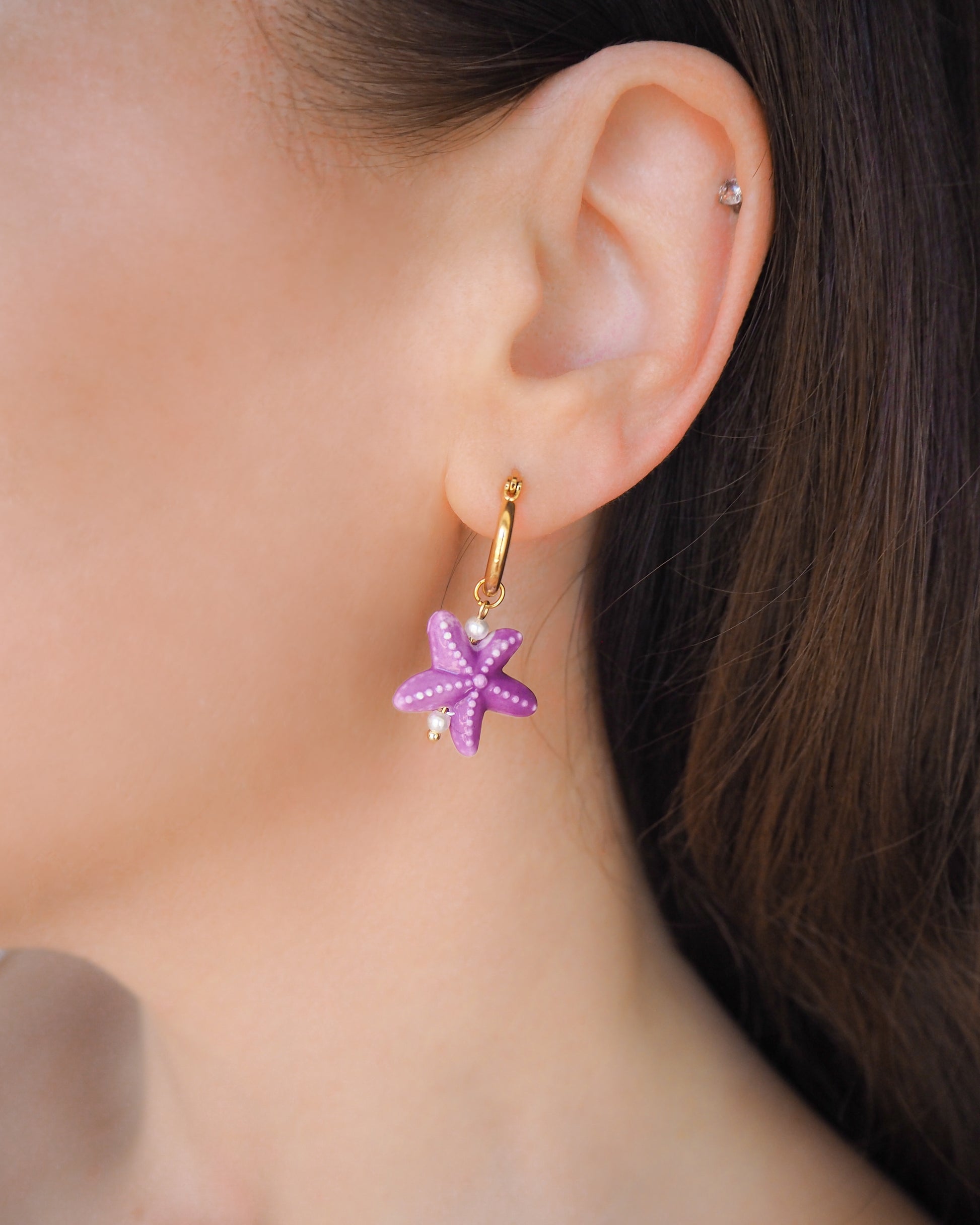 Purple Ceramic Starfish Gold Hoop Earrings in ear model, 14k gold stainless steel hoops with purple ceramic sea star pendants 