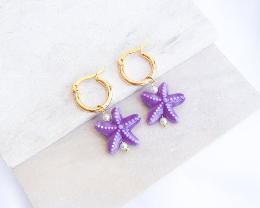 Purple Ceramic Starfish Gold Hoop Earrings on stone displayed, 14k gold stainless steel hoops with purple ceramic sea star pendants 
