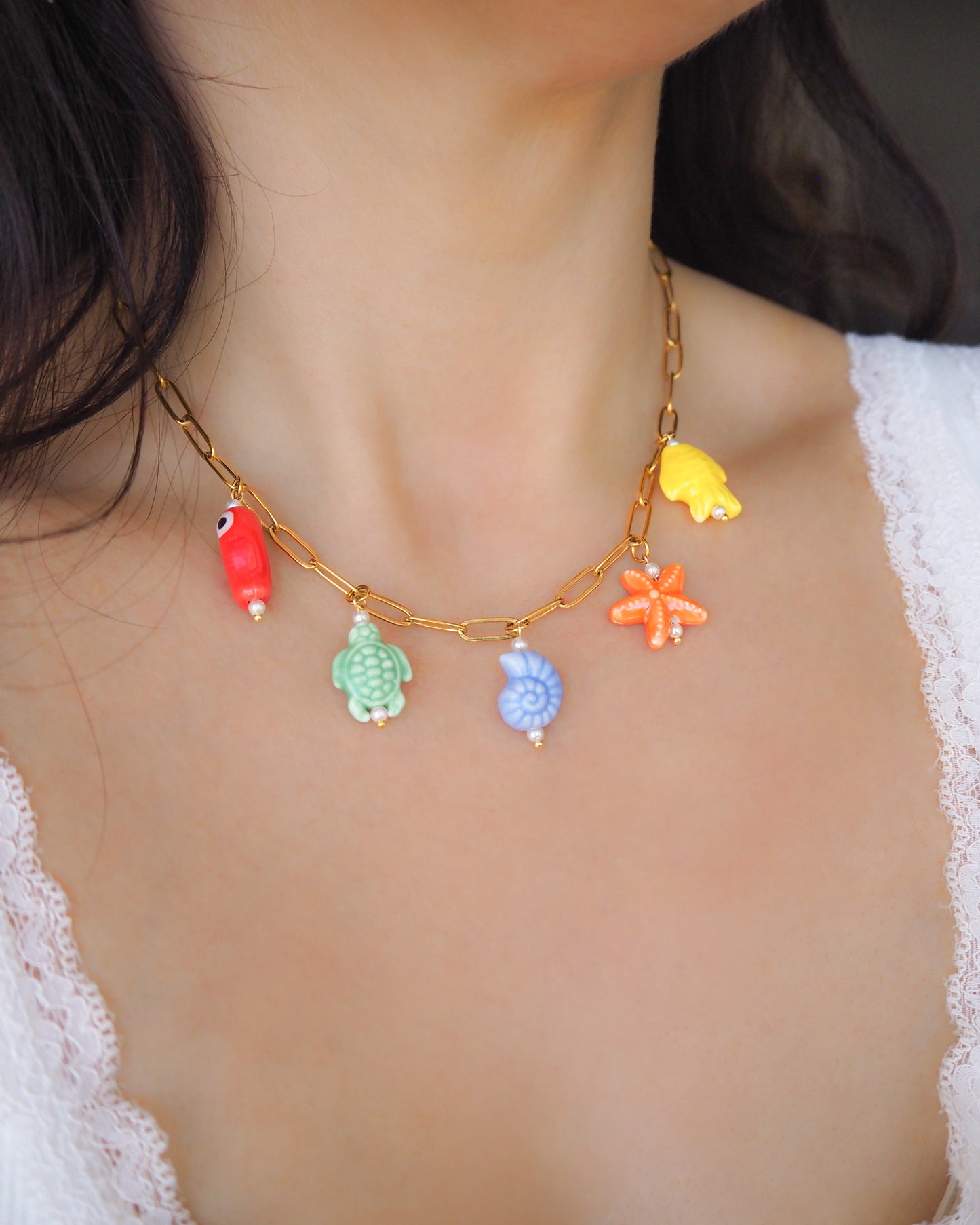 Model wearing Rainbow Ceramic Charm Necklace with 5 ceramic ocean charms (turtle, starfish, fish, shell & more), sea treasure pendants, 18k gold stainless steel chain 