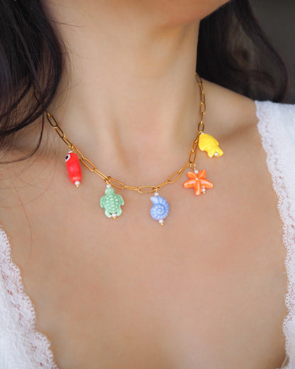 Model wearing Rainbow Ceramic Charm Necklace with 5 ceramic ocean charms (turtle, starfish, fish, shell & more), sea treasure pendants, 18k gold stainless steel chain 