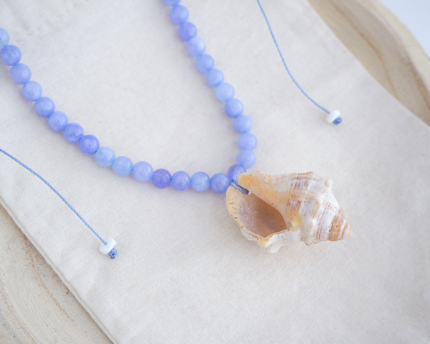 Backside of Red-mouthed Dog Winkle Shell with Angelite Gemstone Necklace on display, Blue gemstone bead necklace with off white big conch shell
