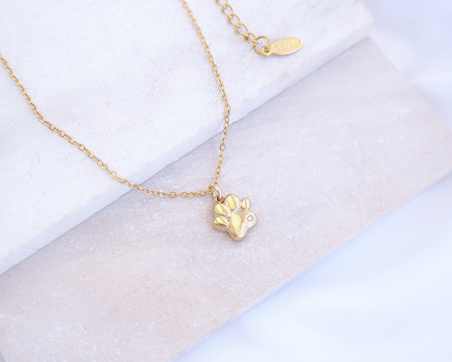 Gold necklace with a paw-shaped pendant on a light background. Tiny Cat Paw Gold Necklace on stone displayed, Memory Cat Jewelry, Gold Cat Necklace 