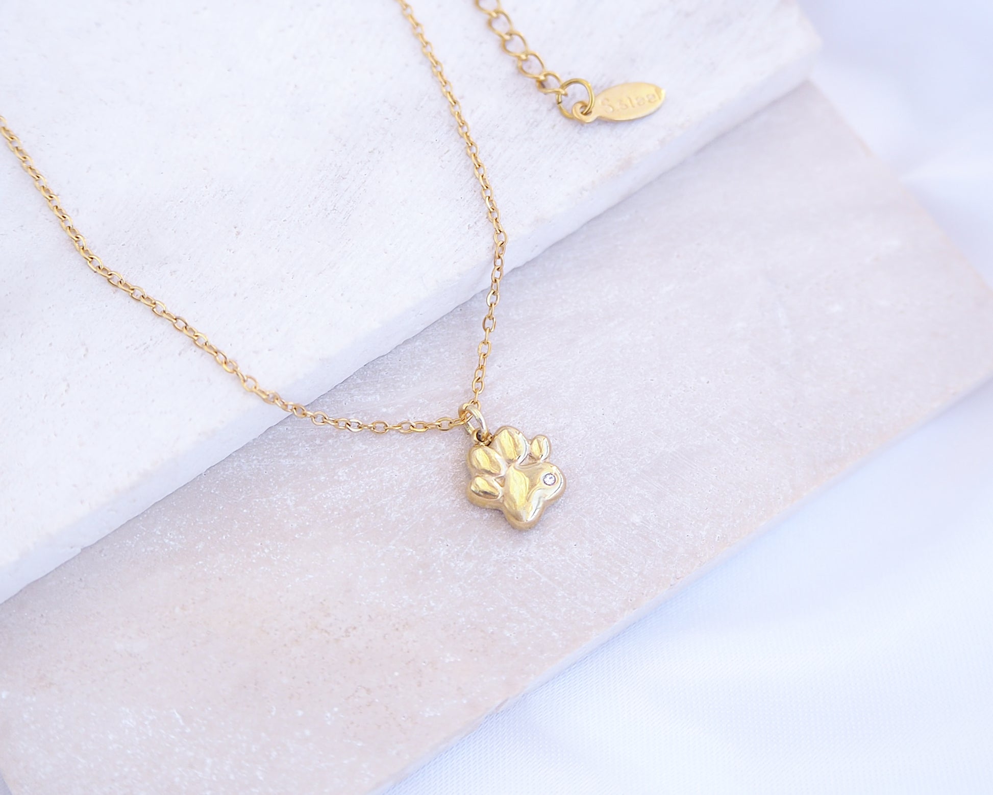 Gold necklace with a paw-shaped pendant on a light background. Tiny Cat Paw Gold Necklace on stone displayed, Memory Cat Jewelry, Gold Cat Necklace 