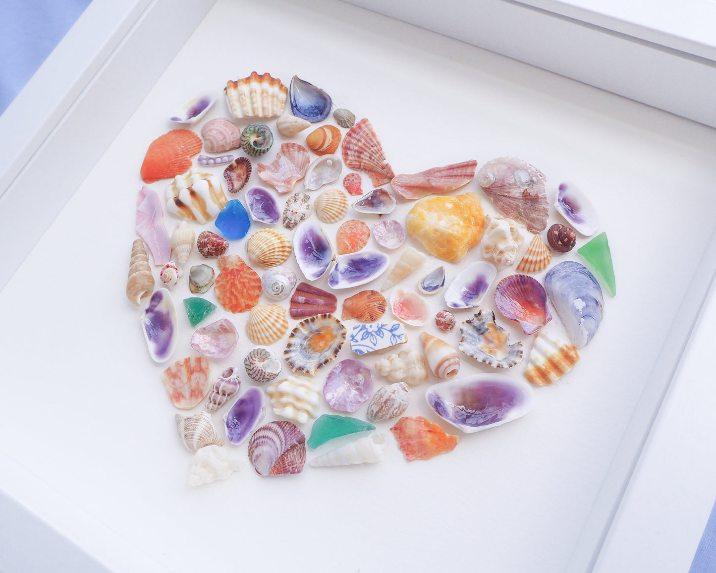 Collection of colorful seashells arranged in a circular pattern on a white surface. Side view of Rainbow Seashell Heart Artwork with colorful shell handpicked from Portugal. Coastal Home Wall Decor, Shell Wall Art, Handmade Shell Artwork, Cute Coastal Nursery Decoration 