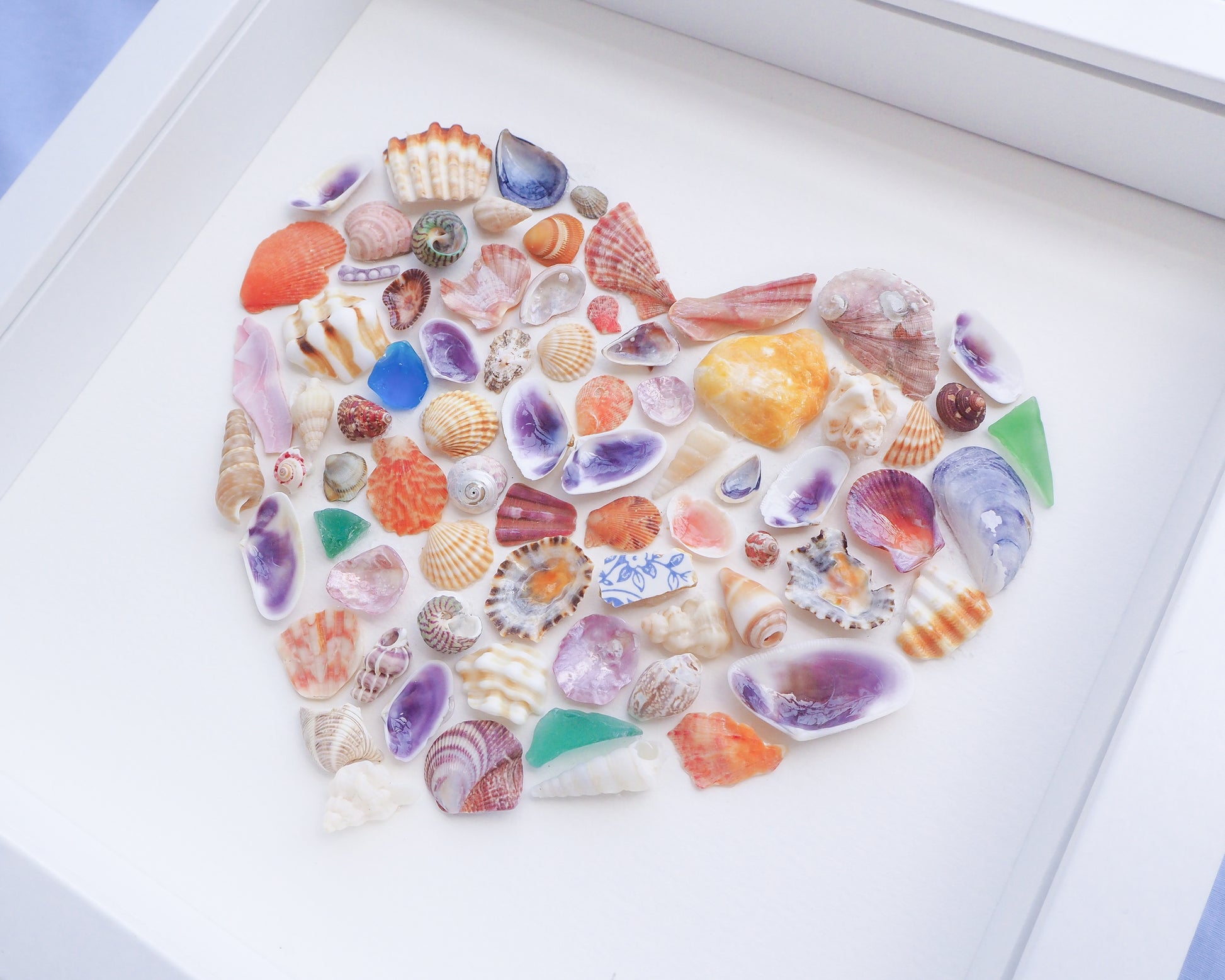 Collection of colorful seashells arranged in a circular pattern on a white surface. Side view of Rainbow Seashell Heart Artwork with colorful shell handpicked from Portugal. Coastal Home Wall Decor, Shell Wall Art, Handmade Shell Artwork, Cute Coastal Nursery Decoration 