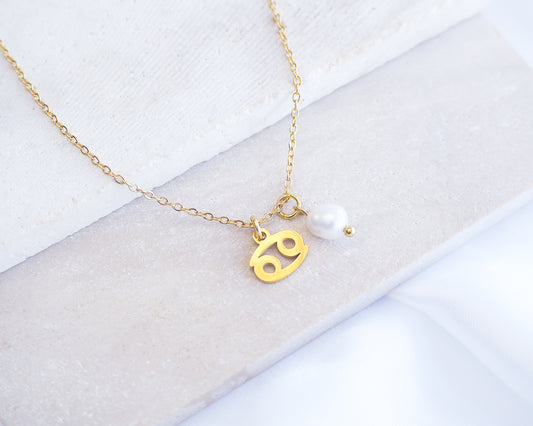 Gold Cancer Zodiac Pearl Necklace on stone displayed, made with 18k gold stainless steel and white freshwater pearl 