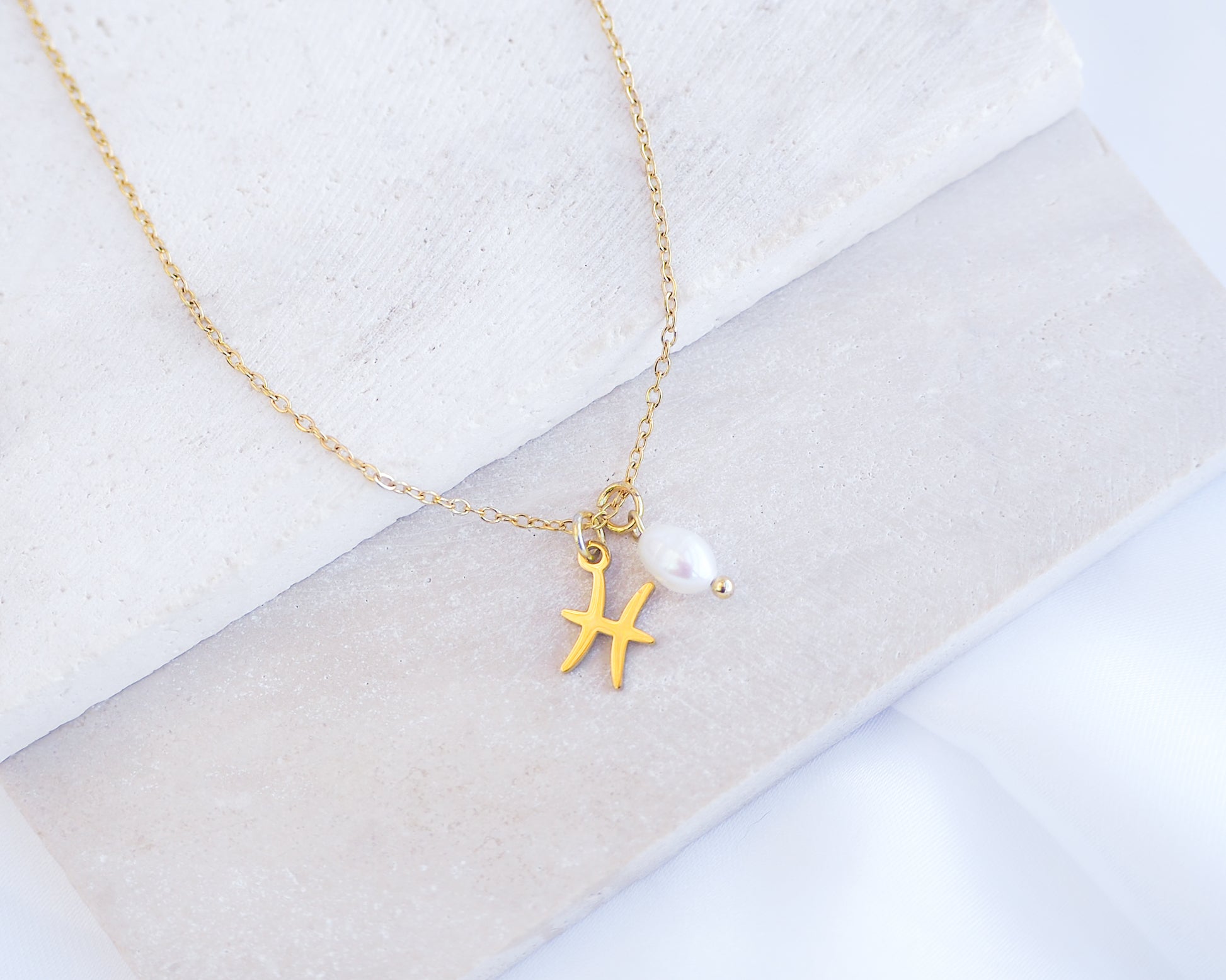 Gold Pisces Zodiac Pearl Necklace on stone displayed, made with 18k gold stainless steel and white freshwater pearl 