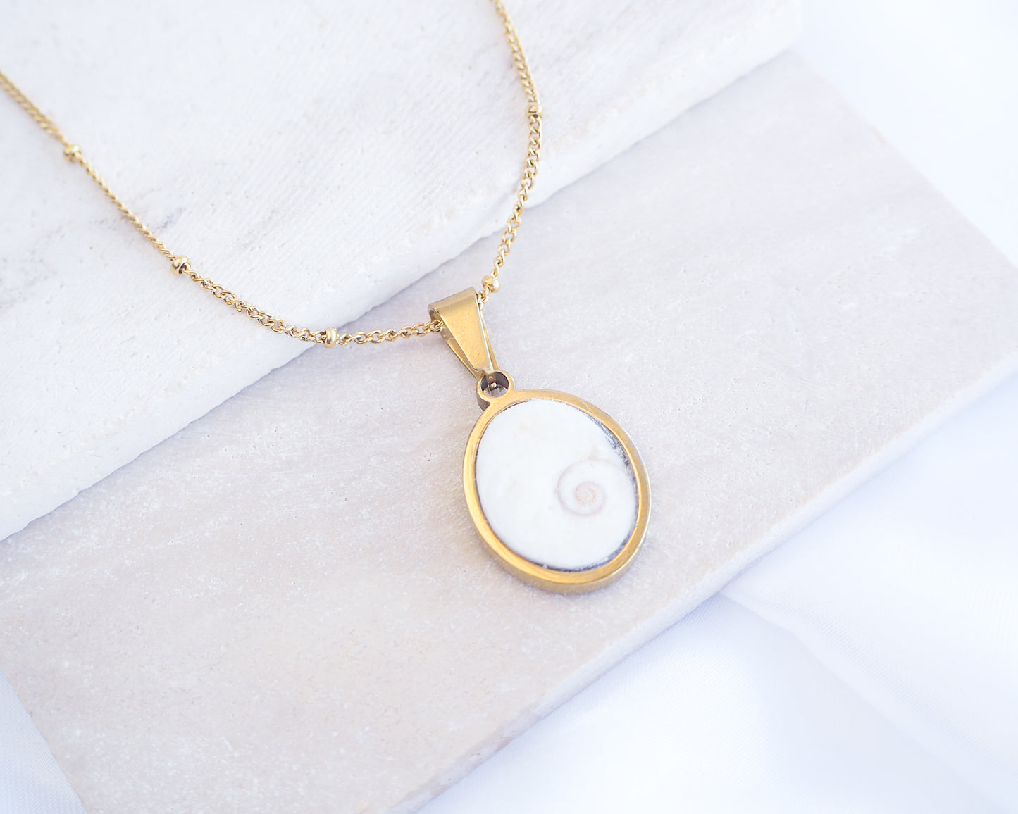 Gold necklace with a pendant on a white background. White Eye of Saint Lucia Gold Necklace on stone displayed, 18k gold stainless steel shiva eye pendant necklace, Saint Lucy Eye, operculum pendant